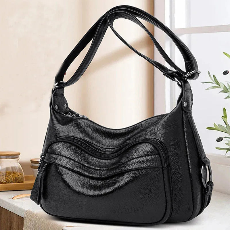 Blue horizontal square women's crossbody bag with a soft handle and zipper opening, showing organiser pockets inside.