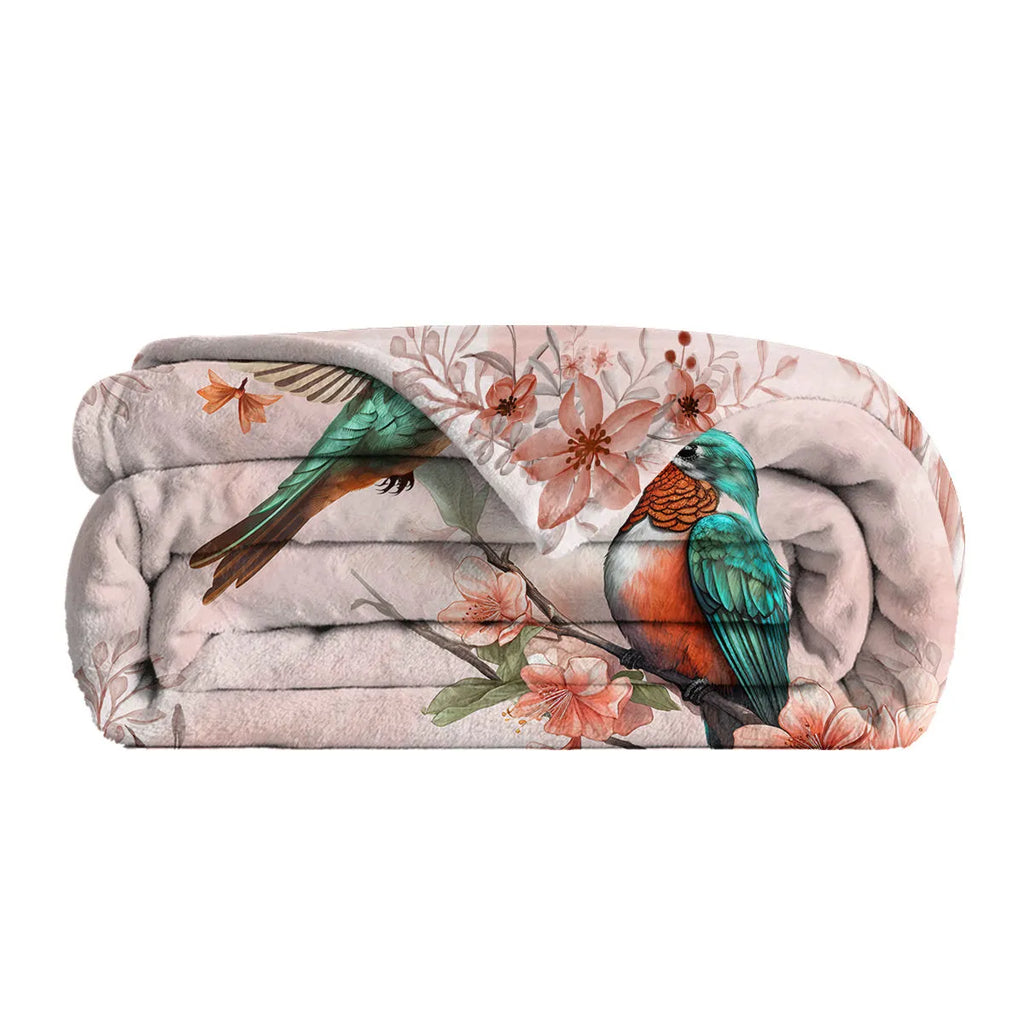 Pink hummingbird floral fleece throw blanket made of soft flannel velvet, folded on a sofa