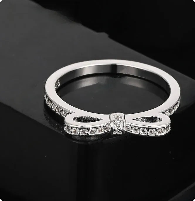 Silver coloured ring with a detailed bow shape set with clear sparkling zircon crystals on a model's hand.