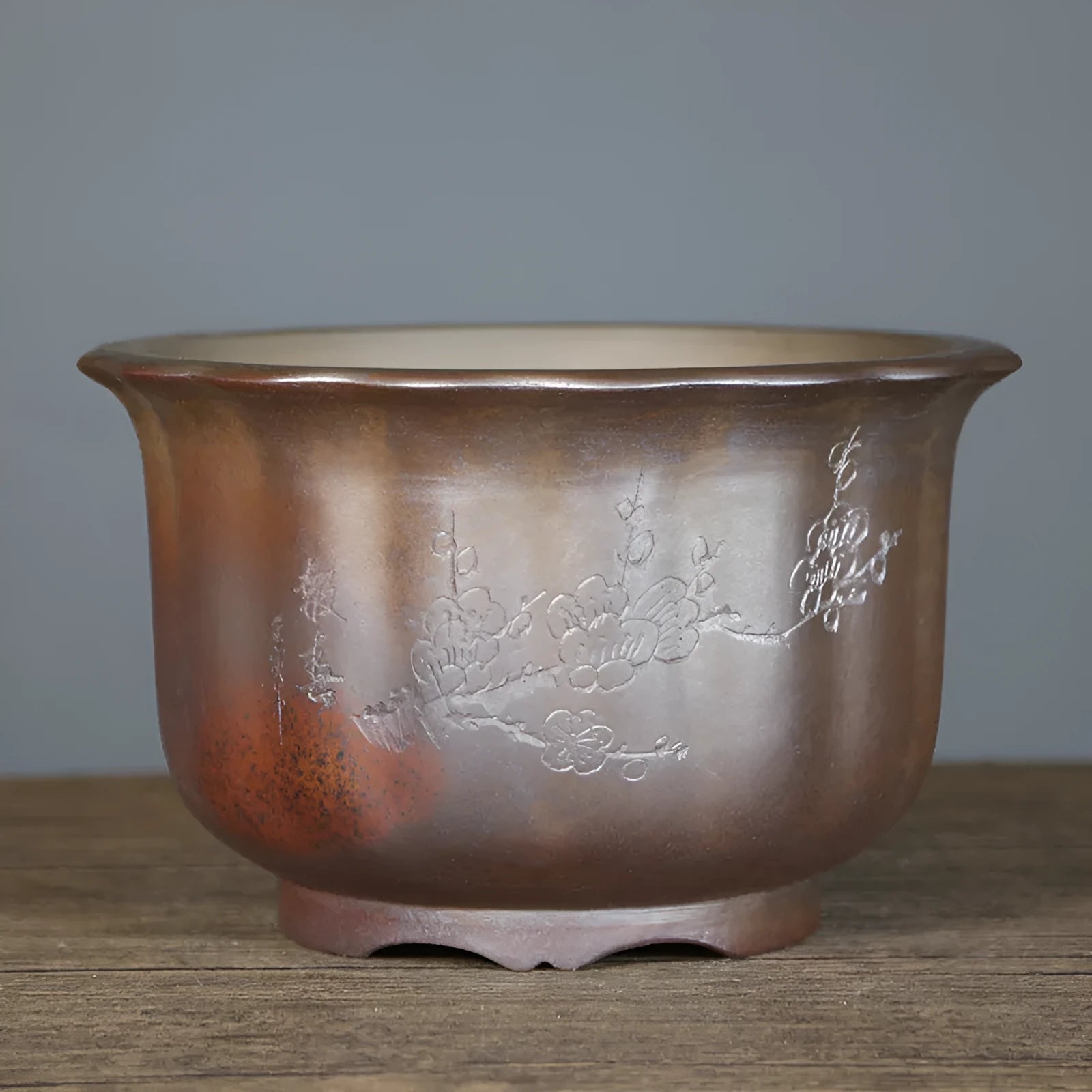 Antique carved ceramic flower pot with wood burning finish on a wooden table.