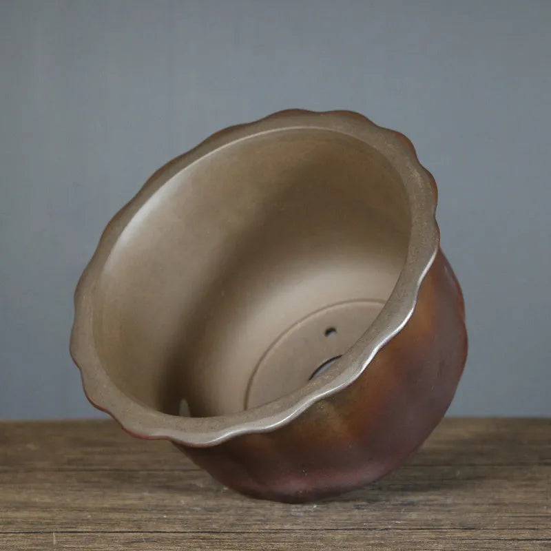 Antique carved ceramic flower pot with wood burning finish on a wooden table.