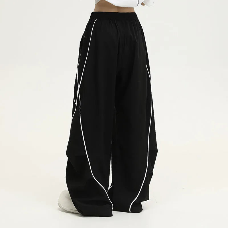 Black sports trousers with white stripes, showing wide-leg loose fit and mid-waist design.