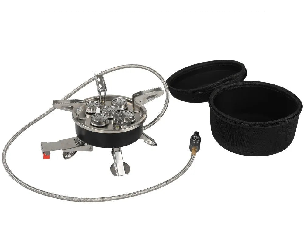 Silver portable folding camping stove with extended copper gas hose, shown on a wooden picnic table.