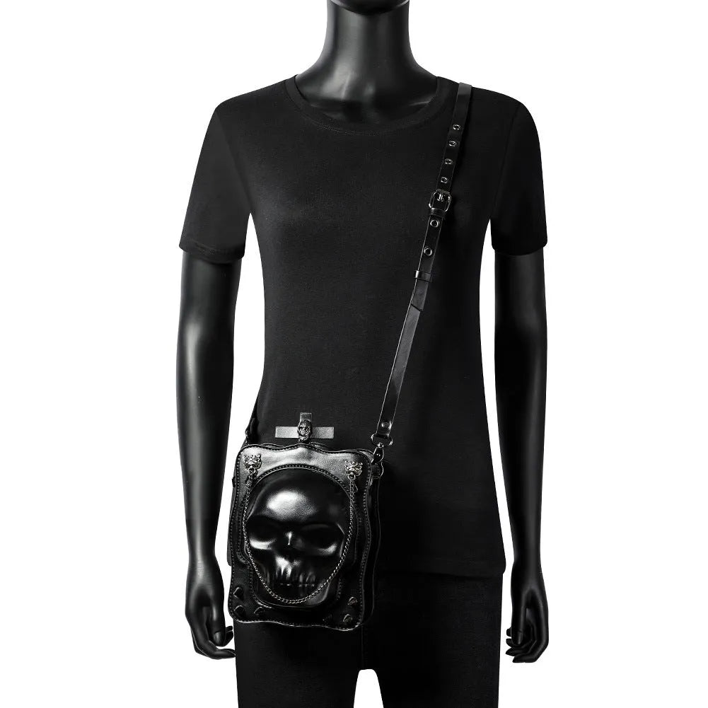 Black mini square crossbody bag with embossed skull design, metal chain strap, and zip opening.