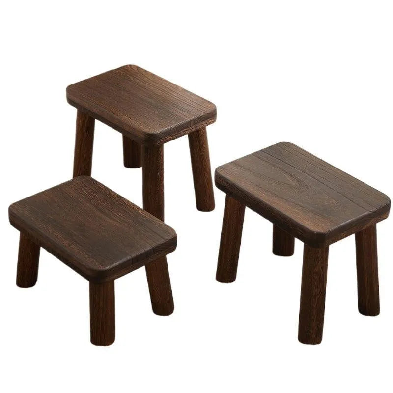 Distressed solid wood shoe changing stool with bracket legs in a living room setting.