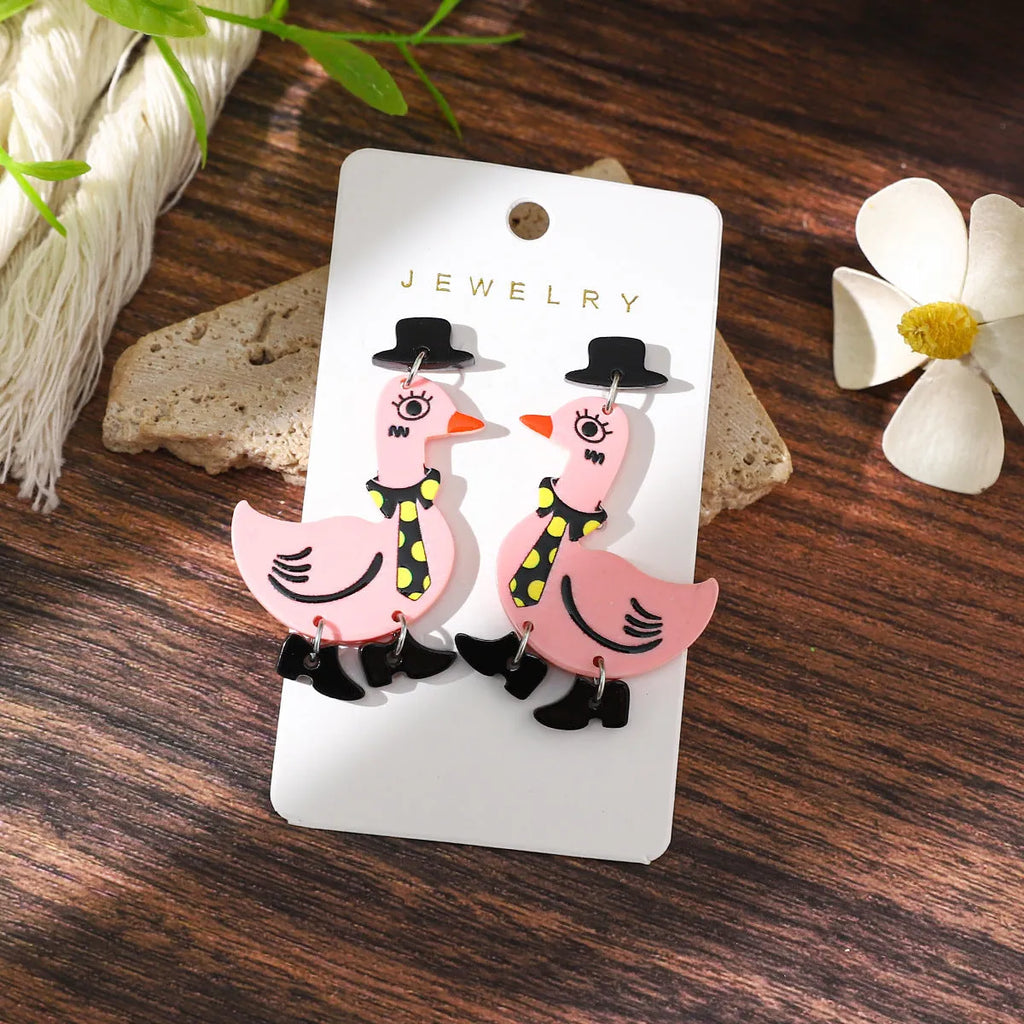 Three pairs of acrylic cartoon duck earrings in pink, white, and yellow on a light background