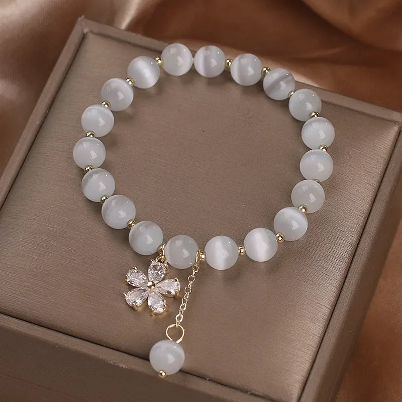 Close-up of a women's white cat's eye crystal bracelet with a flower tassel and silver safety buckle.