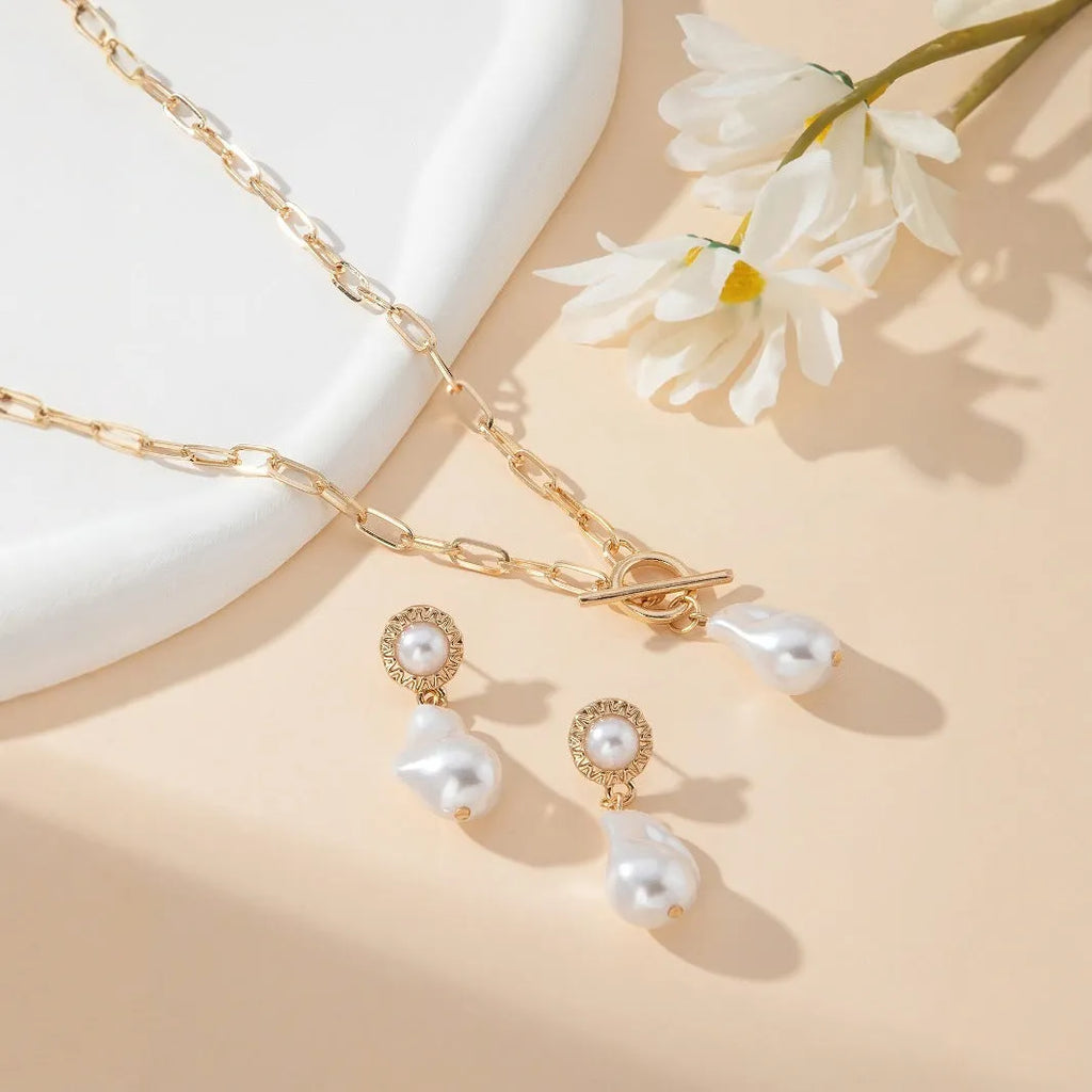 Gold-coloured baroque pearl pendant necklace and earring set on a dark background.