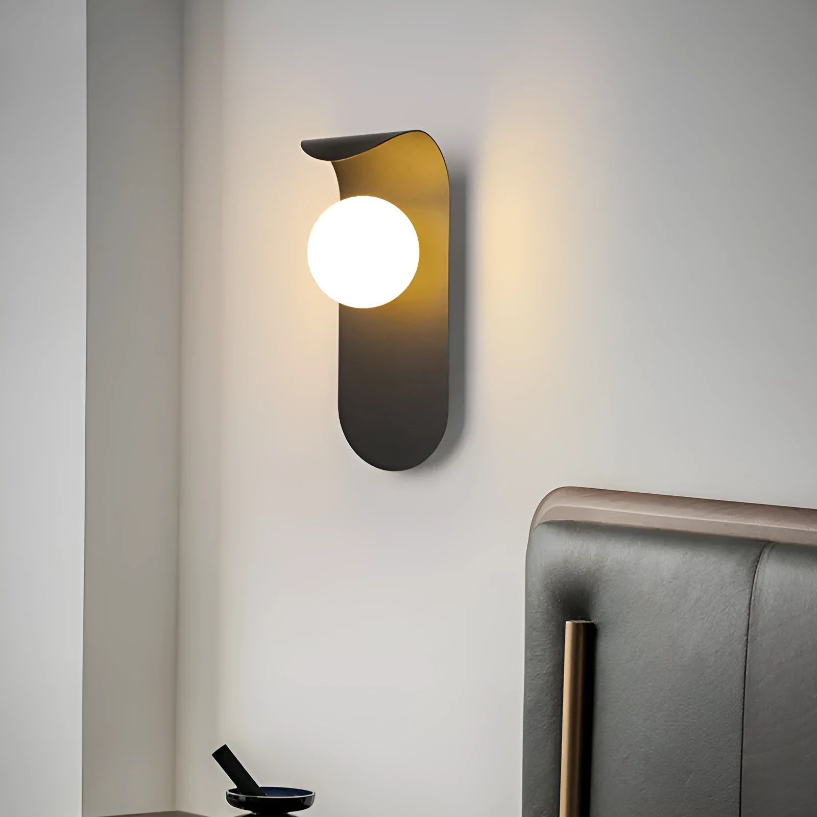 Modern minimalist wall lamp in black finish with LED warm light on a bedroom wall beside bed