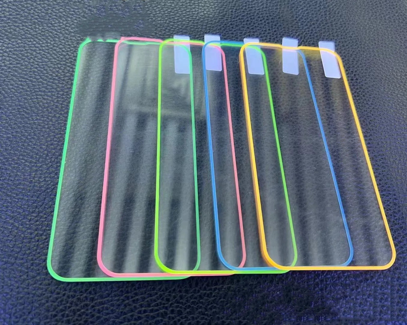 Fluorescent pink tempered glass screen protector glowing on an iPhone 13 in a dark room.