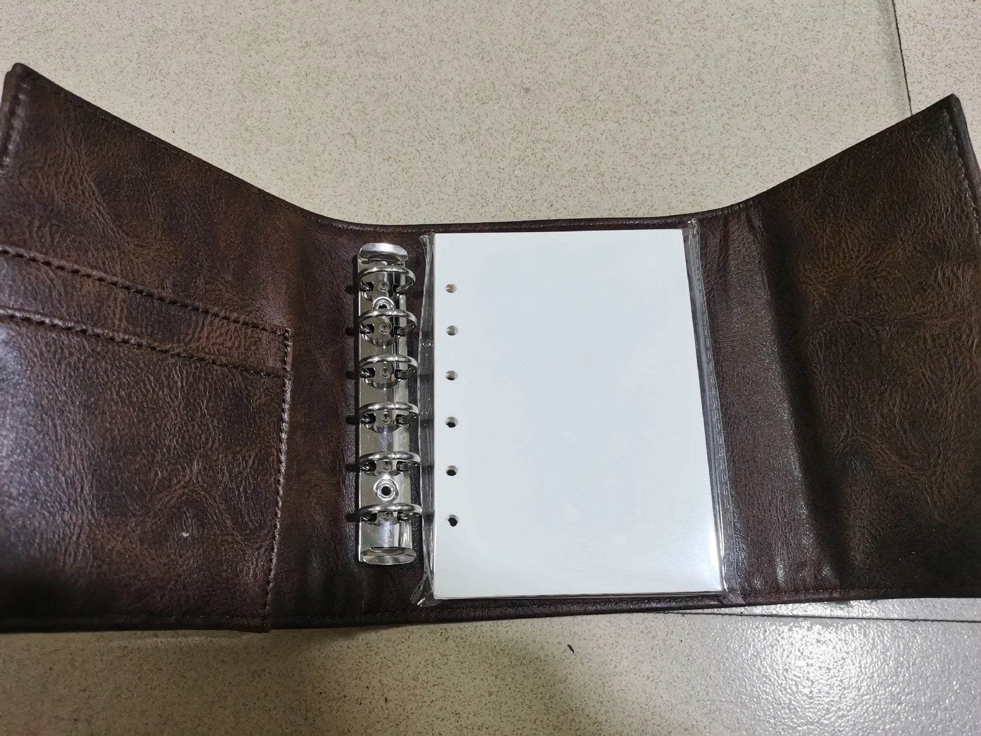 Brown retro-style A7 notebook with a PU leather-look cover and metal buckle closure, showing loose-leaf binding.