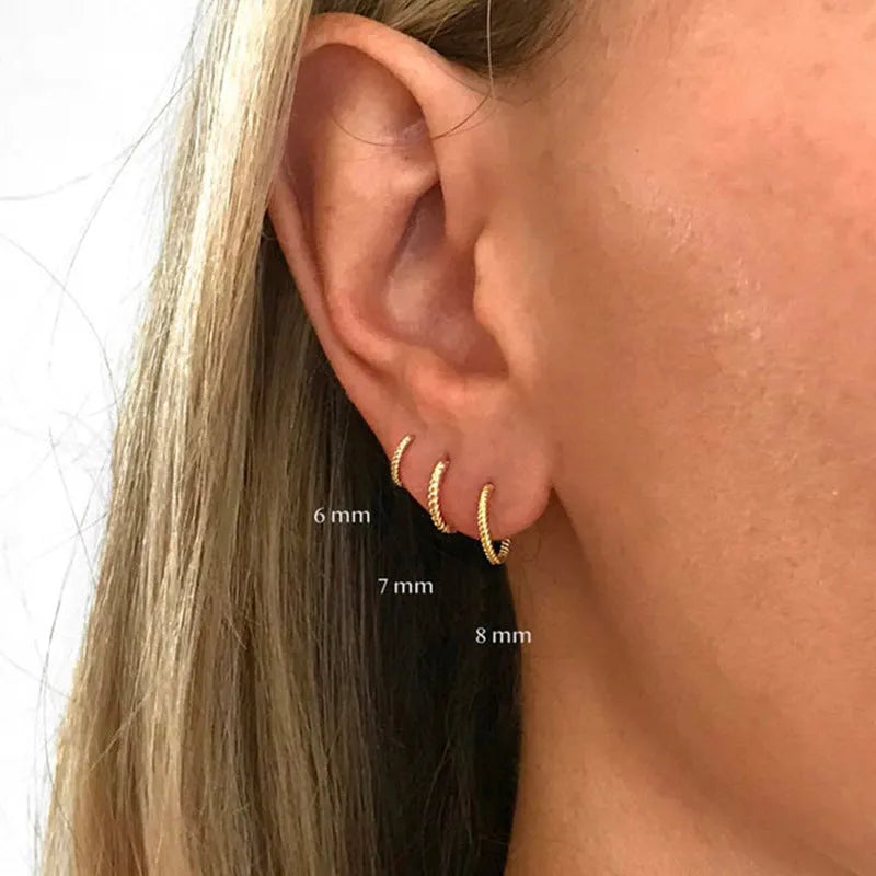 Close-up of a twisted sterling silver round hoop earring in gold colour, showing geometric design.