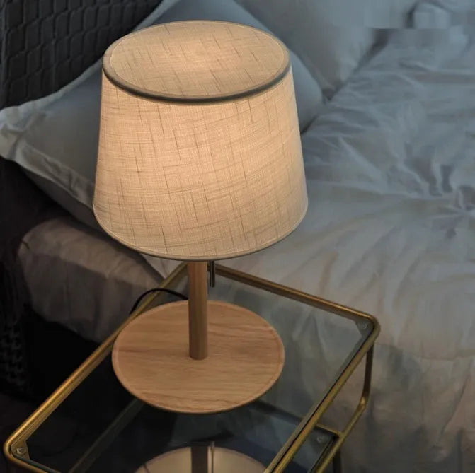 Walnut-coloured solid wood bedside lamp with a white cloth shade on a wooden surface.