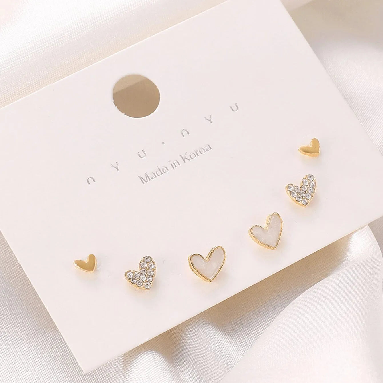 Three pairs of heart-shaped earrings in gold, black, black-white, and pink colours on display