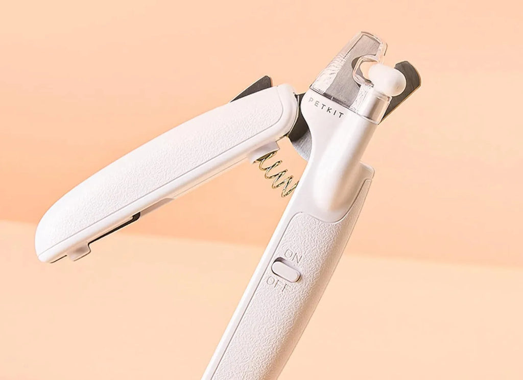 White pet nail clippers with LED light and transparent anti-splash guard next to a nail file on a table