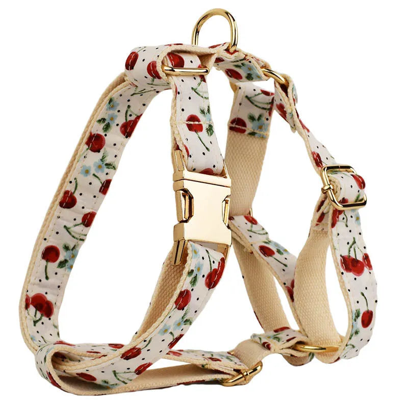Red cherry print dog collar and leash set with light gold buckle, matching bow, vest, and poop bag.