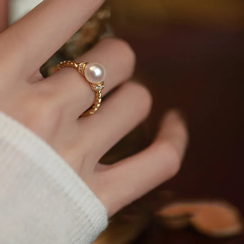 Antique-style twisted copper ring with a central white pearl, shown on a finger, adjustable band visible.