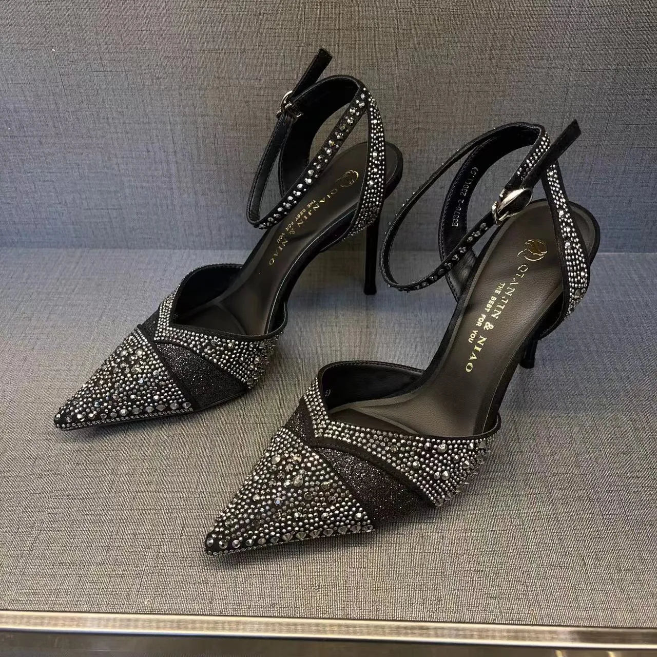 Women's silver and black hollow stiletto high heels with pointed toe and red sole on a plain background.
