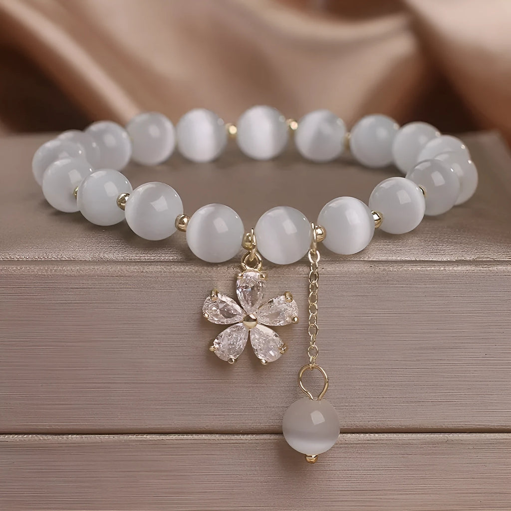 Close-up of a women's white cat's eye crystal bracelet with a flower tassel and silver safety buckle.