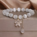 Close-up of a women's white cat's eye crystal bracelet with a flower tassel and silver safety buckle.