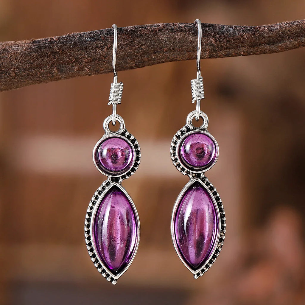 Close-up of vintage black and purple geometric drop earrings with a circular pendant on a long chain.