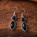 Close-up of vintage black and purple geometric drop earrings with a circular pendant on a long chain.