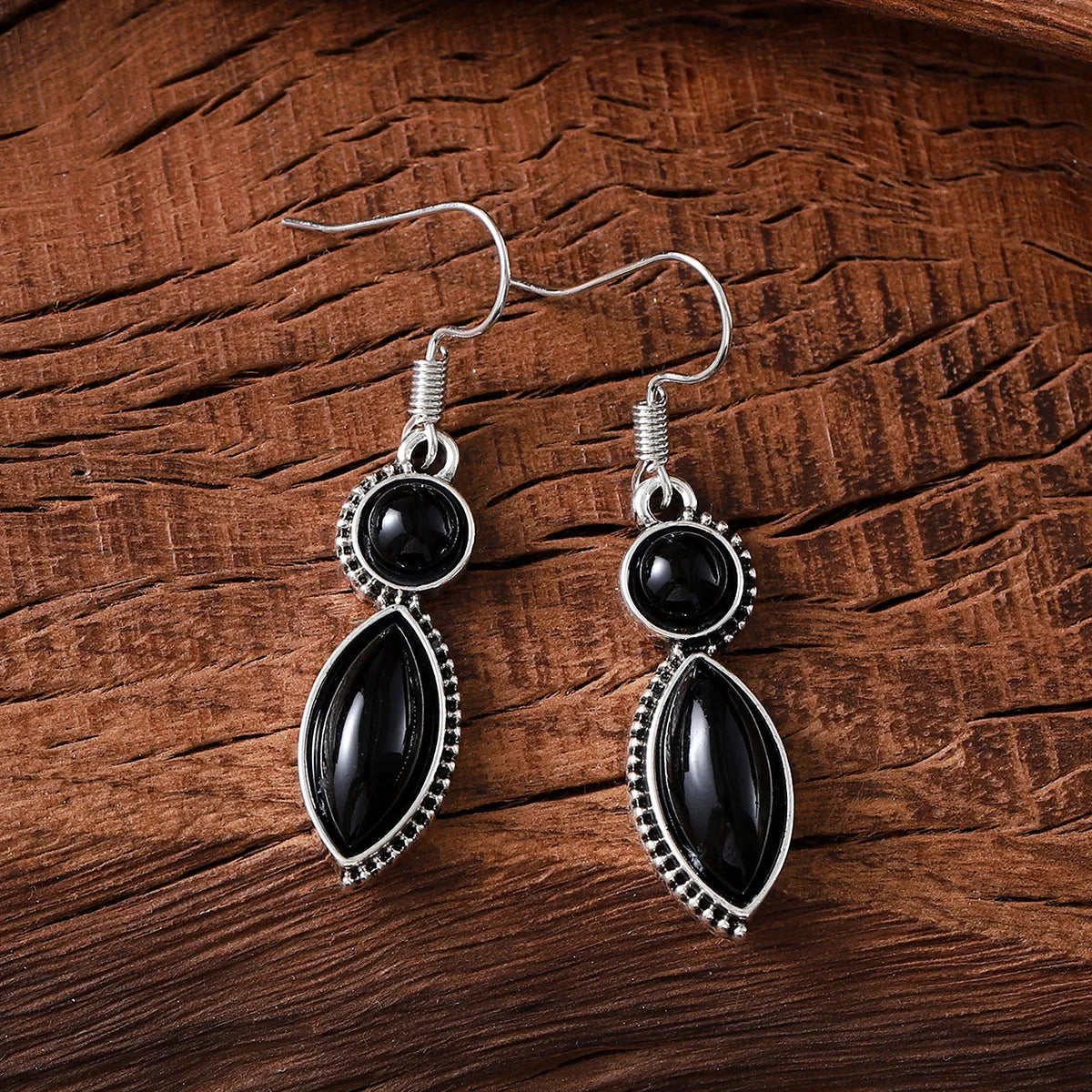 Close-up of vintage black and purple geometric drop earrings with a circular pendant on a long chain.