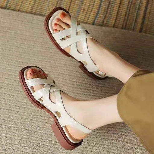 Women's black patent leather square toe sandals with a cross strap and low heel on a white background.