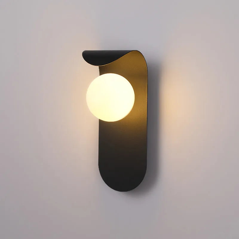Modern minimalist wall lamp in black finish with LED warm light on a bedroom wall beside bed
