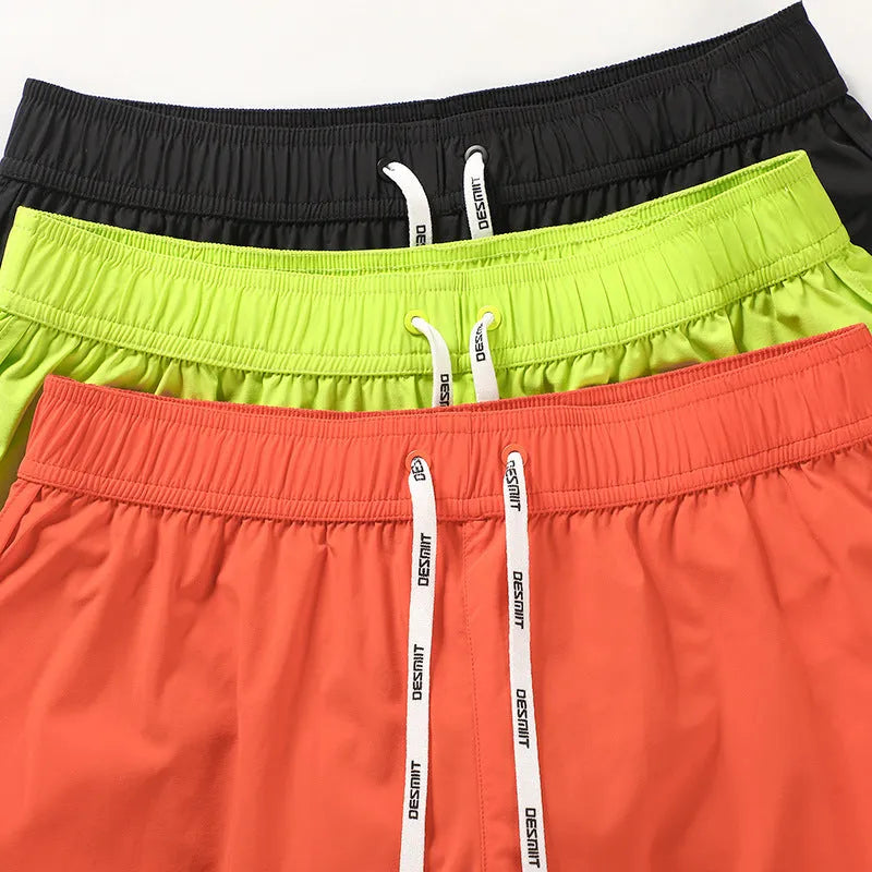 Men's loose-fit polyester beach shorts in orange, fluorescent green, and black on a size chart background.