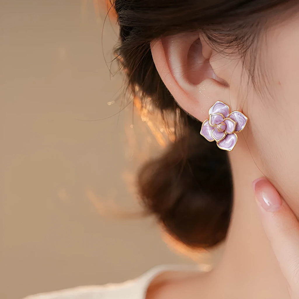 Close-up of gold plated purple flower stud earrings with iridescent oil-spot glaze on a copper base.