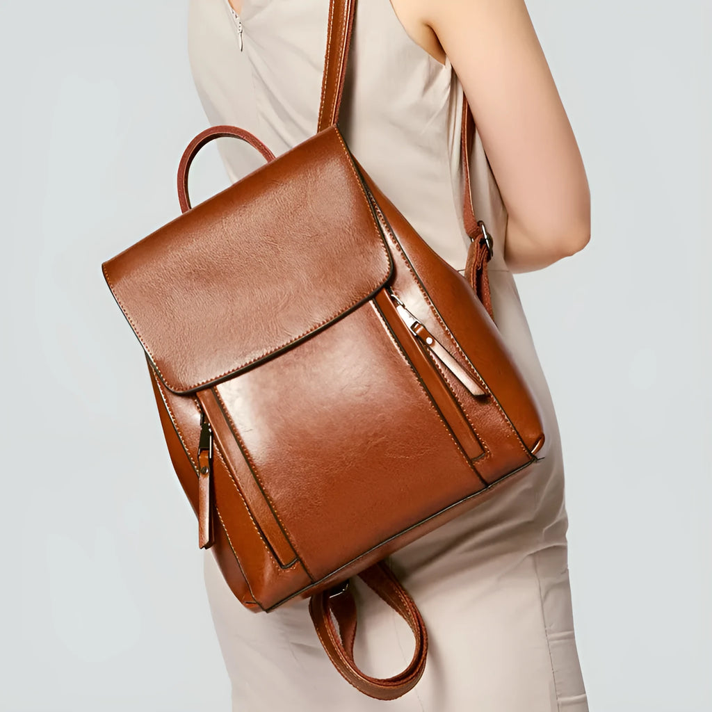 Brown oil-waxed cowhide leather women's backpack with flap closure, showing internal document pocket and stitching detail.