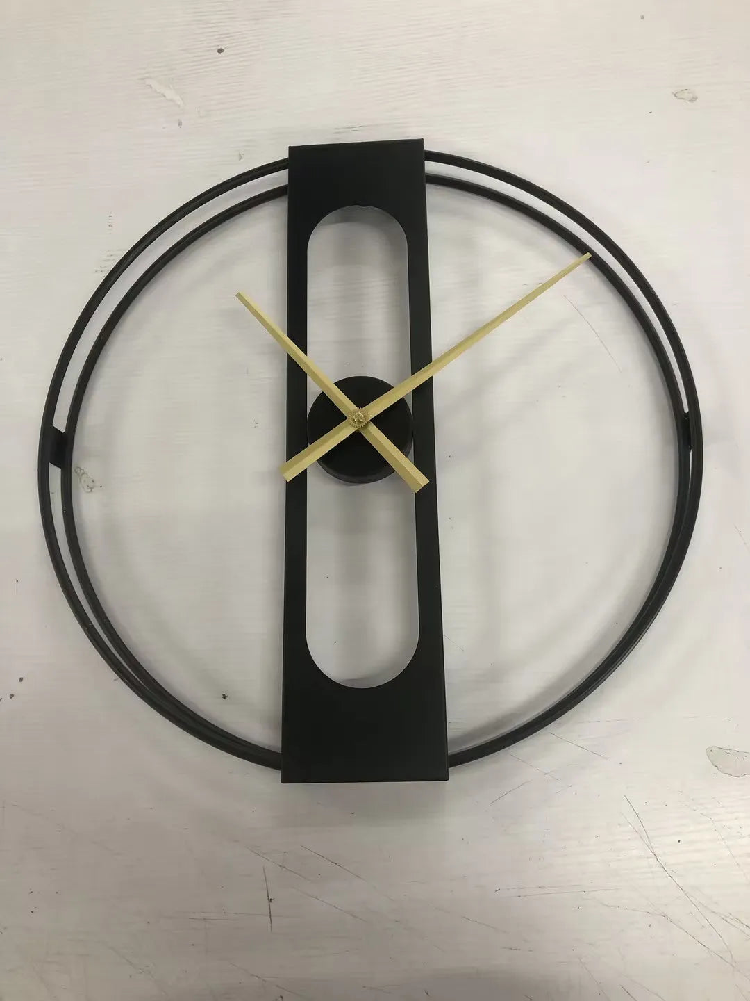 Large round metal wall clock with Roman numerals on a white wall.