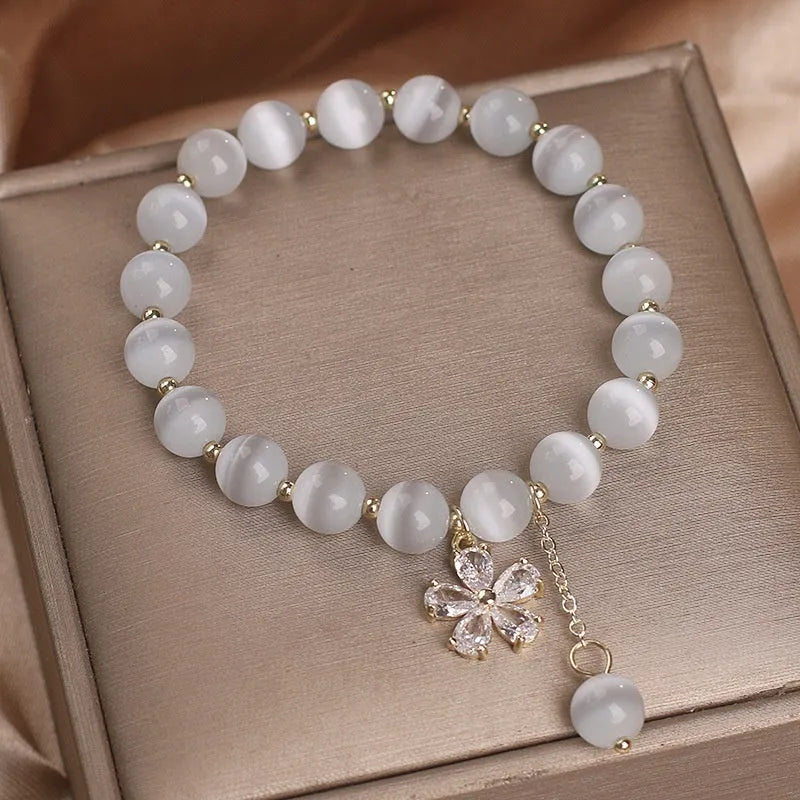 Close-up of a women's white cat's eye crystal bracelet with a flower tassel and silver safety buckle.