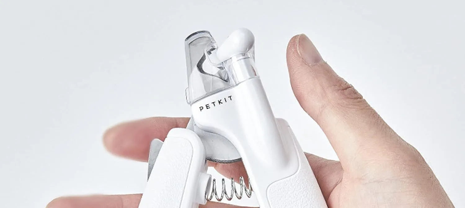 White pet nail clippers with LED light and transparent anti-splash guard next to a nail file on a table