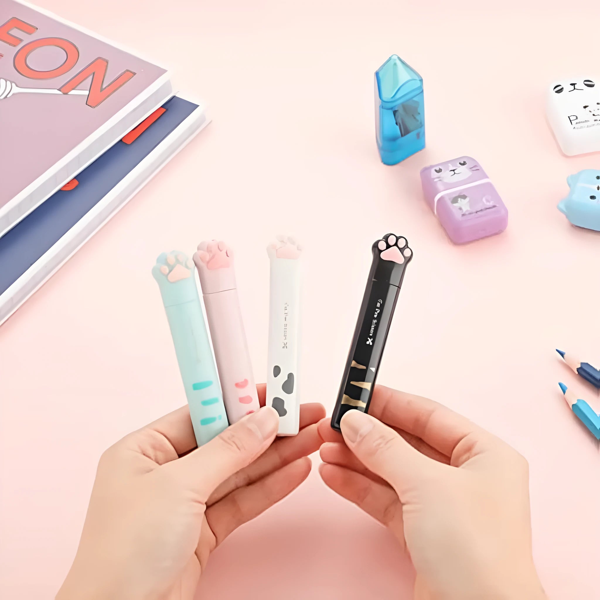 Set of four mini folding scissors with cat paw design in black, blue, pink, and white colours on a plain surface.