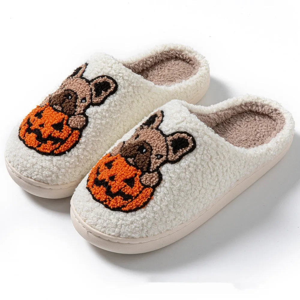 Black Halloween slippers with pumpkin print, plush fabric, and thick textured TPR rubber soles on a wooden floor.