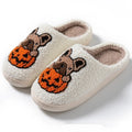 Black Halloween slippers with pumpkin print, plush fabric, and thick textured TPR rubber soles on a wooden floor.