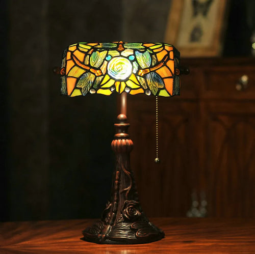 Colourful Tiffany-style stained glass table lamp with resin base on a wooden desk.