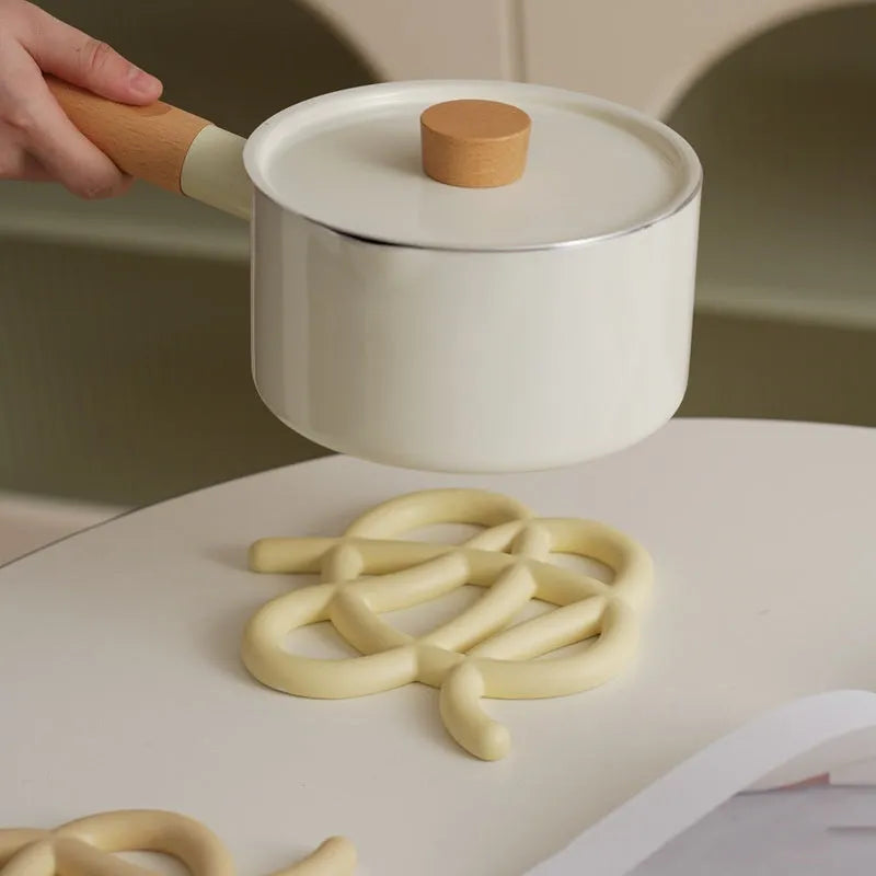 Modern irregular-shaped ceramic heat proof mat in grey on a wooden table protecting it from a hot pan.