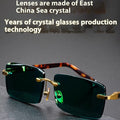 Frameless dark green crystal sunglasses with metal arms on a table next to their hard case.