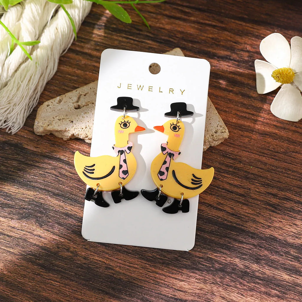 Three pairs of acrylic cartoon duck earrings in pink, white, and yellow on a light background