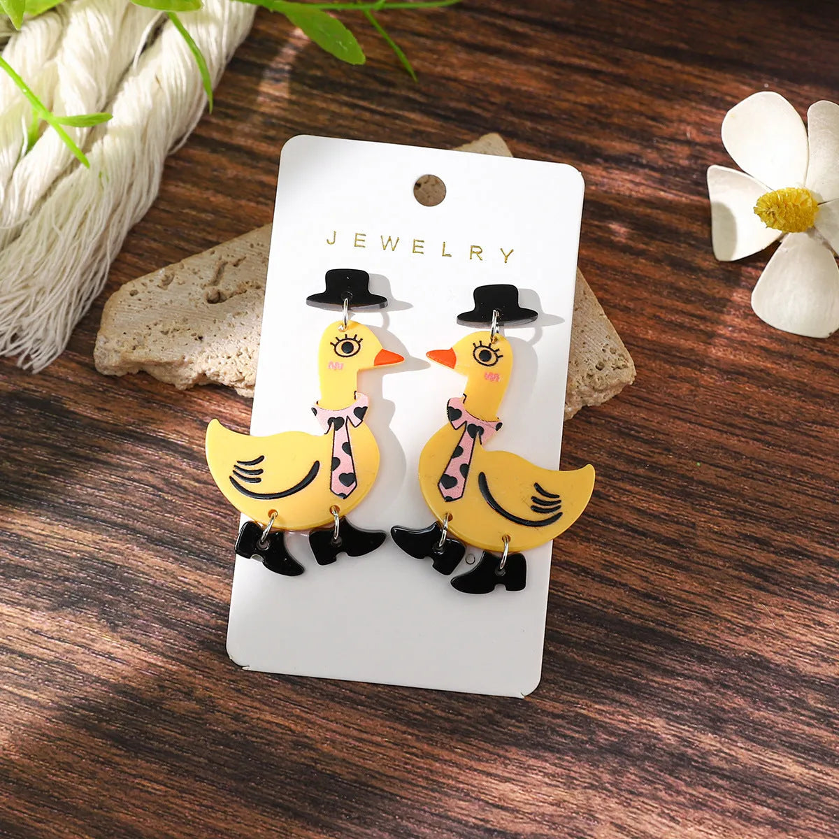 Three pairs of acrylic cartoon duck earrings in pink, white, and yellow on a light background