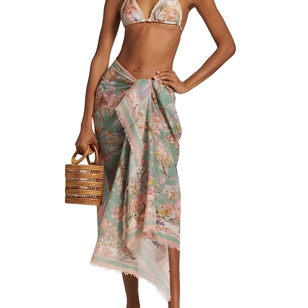 Women's creamy-white floral bikini swimsuit set with matching skirt on a beach background.