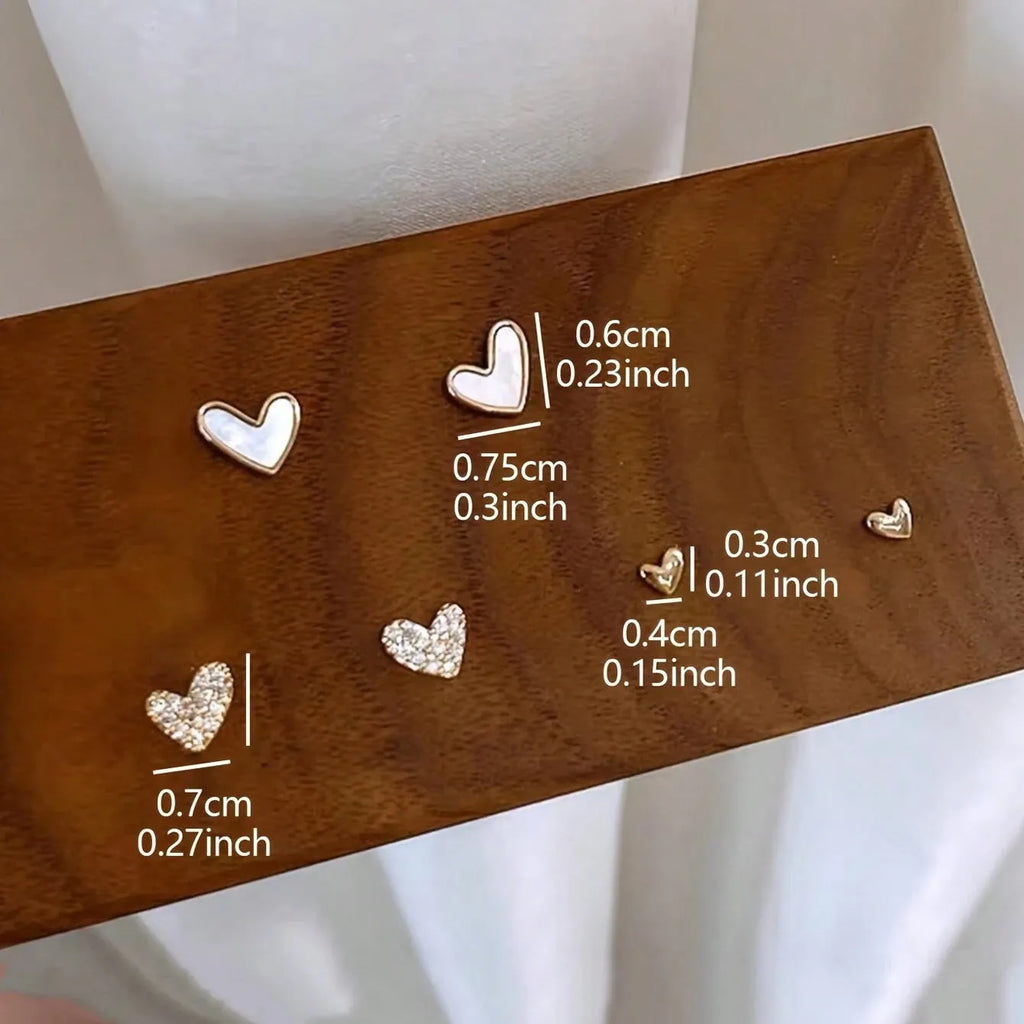 Three pairs of heart-shaped earrings in gold, black, black-white, and pink colours on display