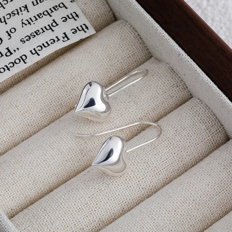 Silver coloured heart-shaped earrings with a glossy three-dimensional design on a white background.