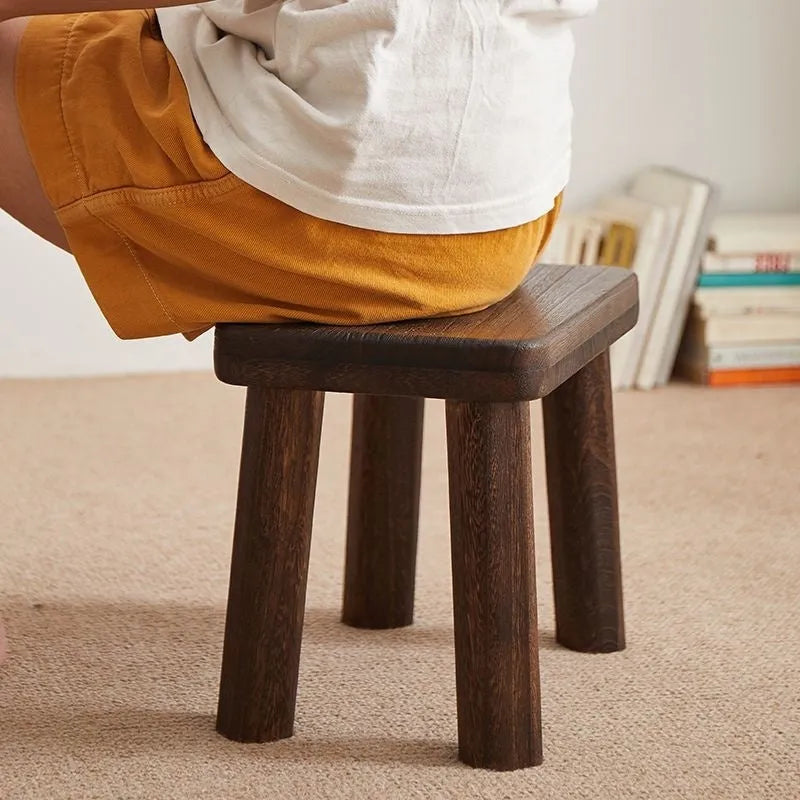 Distressed solid wood shoe changing stool with bracket legs in a living room setting.