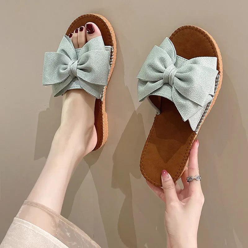 Women's beige slip-on cloth sandals with a bow on the upper and a soft flat rubber sole.