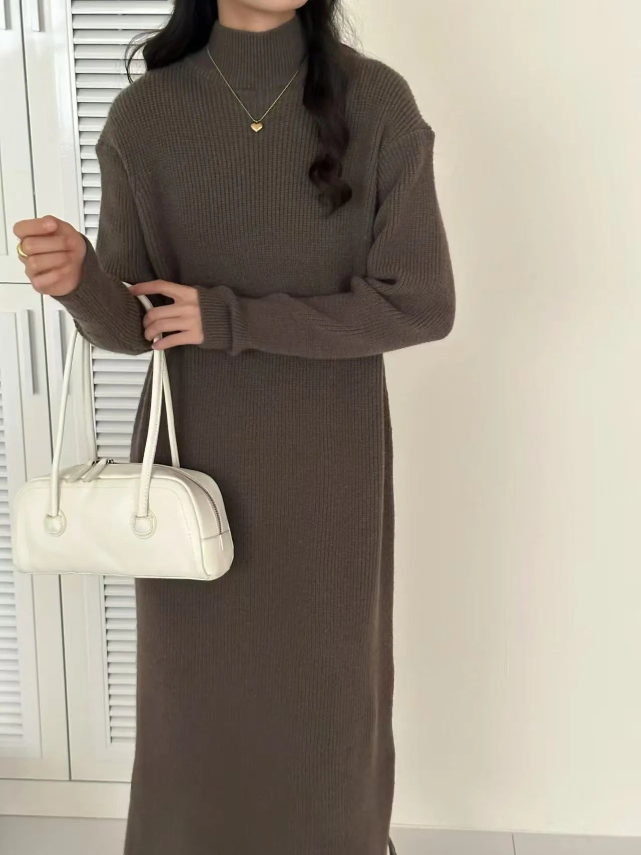 Woman wearing a milky white half turtleneck long sleeve knitted midi dress with a high waist.