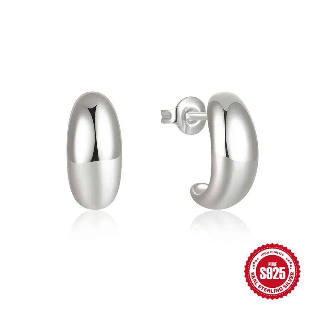 Close-up of a glossy C-shaped sterling silver stud earring on a gold background.